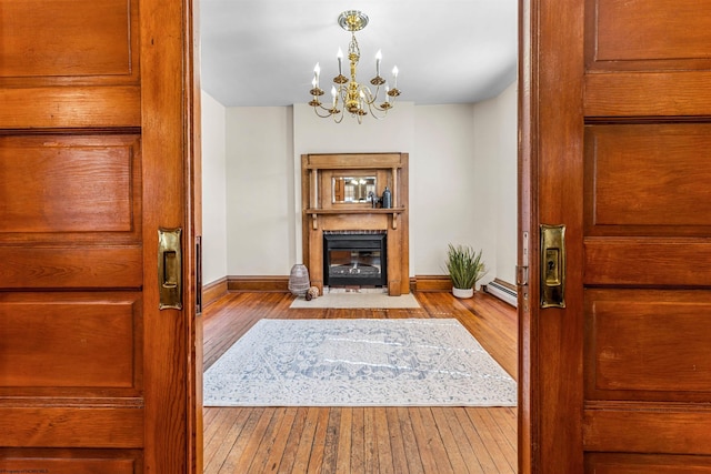 entrance foyer with a fireplace with flush hearth, a baseboard heating unit, wood-type flooring, baseboards, and a chandelier