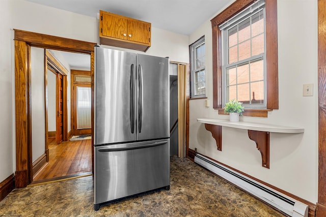 kitchen featuring a wealth of natural light, baseboard heating, brown cabinetry, and freestanding refrigerator