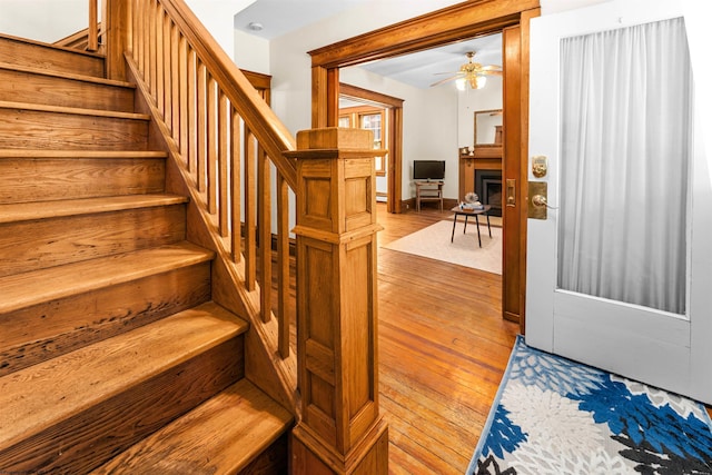 staircase featuring a fireplace, baseboards, wood-type flooring, and ceiling fan