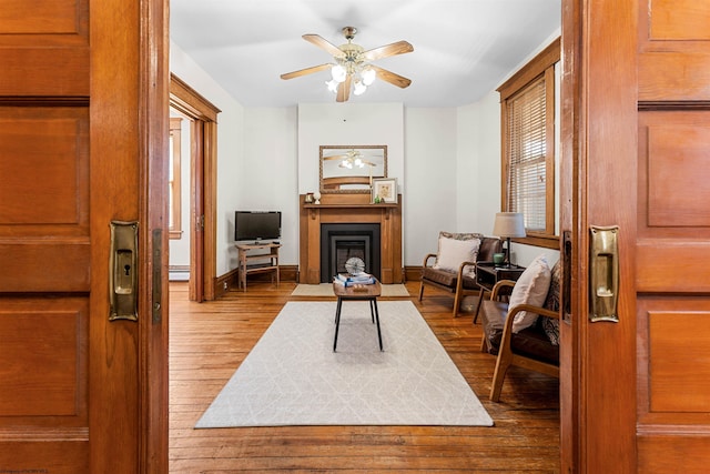 sitting room featuring a fireplace with flush hearth, wood-type flooring, baseboards, and a ceiling fan