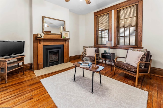 living area featuring a fireplace with flush hearth, baseboards, ceiling fan, and wood-type flooring