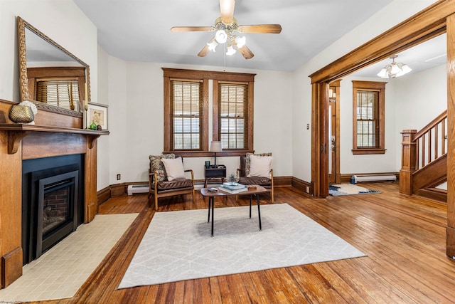 living room with a baseboard heating unit, baseboards, ceiling fan, a fireplace with flush hearth, and wood-type flooring