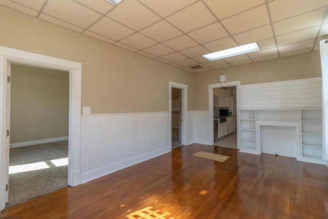 unfurnished living room with a drop ceiling, visible vents, a wainscoted wall, and wood finished floors