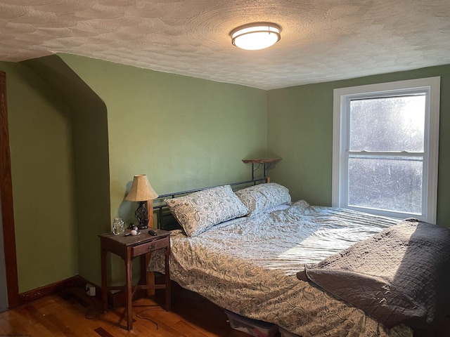 bedroom featuring baseboards, a textured ceiling, and wood finished floors