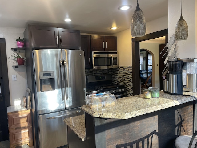 kitchen with tasteful backsplash, dark brown cabinets, a breakfast bar, appliances with stainless steel finishes, and arched walkways