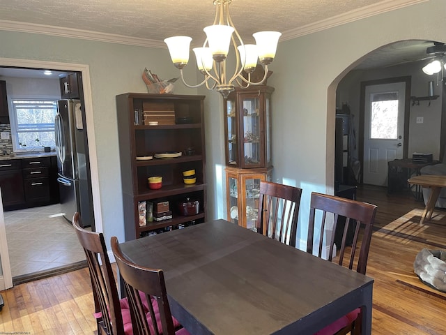 dining space with a textured ceiling, arched walkways, light wood-style floors, crown molding, and a chandelier