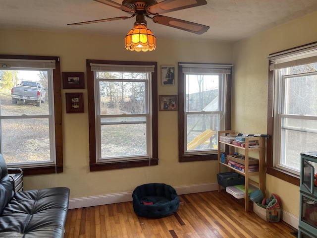 living area with baseboards, a ceiling fan, and hardwood / wood-style floors