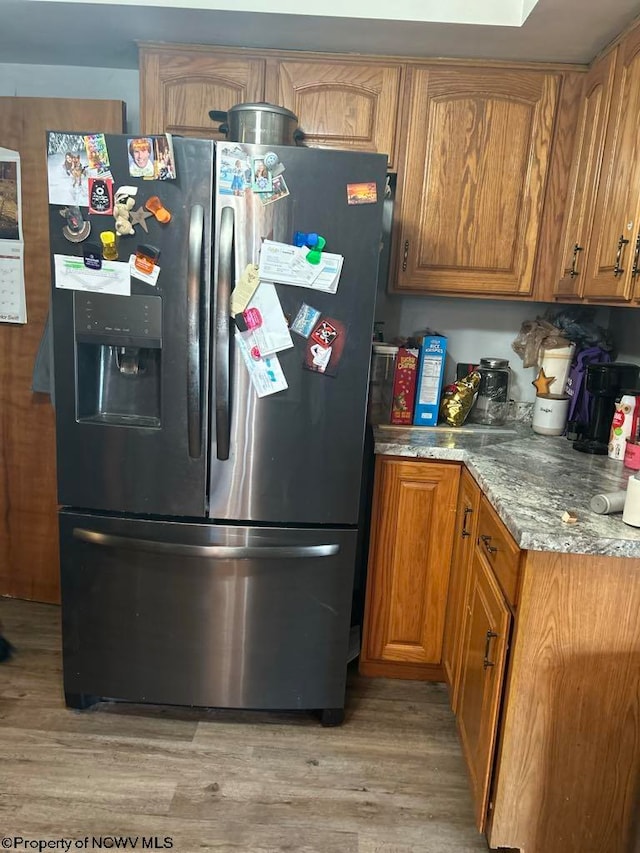 kitchen featuring light stone counters, brown cabinets, light wood-style floors, and stainless steel fridge with ice dispenser