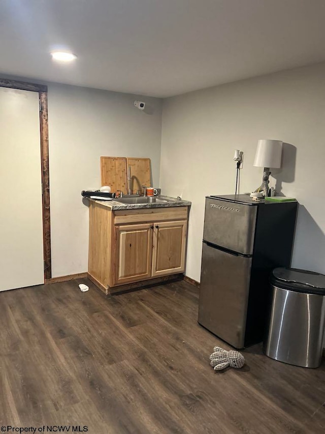 kitchen with dark wood-type flooring, baseboards, freestanding refrigerator, and a sink