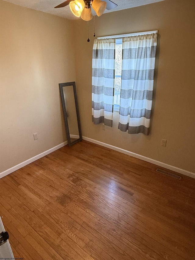 spare room featuring visible vents, wood finished floors, baseboards, and ceiling fan