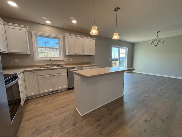 kitchen with wood finished floors, electric range, a sink, light countertops, and stainless steel dishwasher