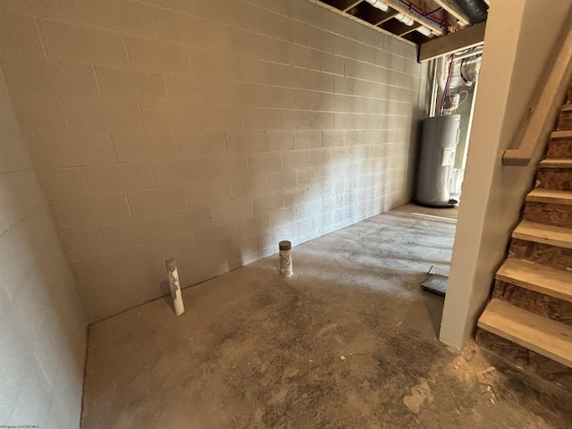 unfinished basement with concrete block wall, electric water heater, and stairs