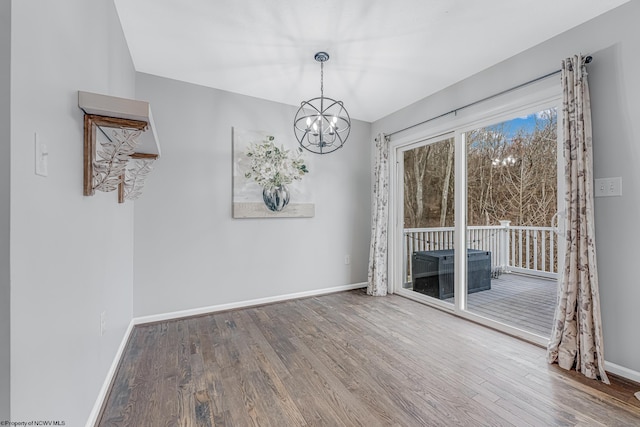 unfurnished dining area featuring an inviting chandelier, wood finished floors, and baseboards