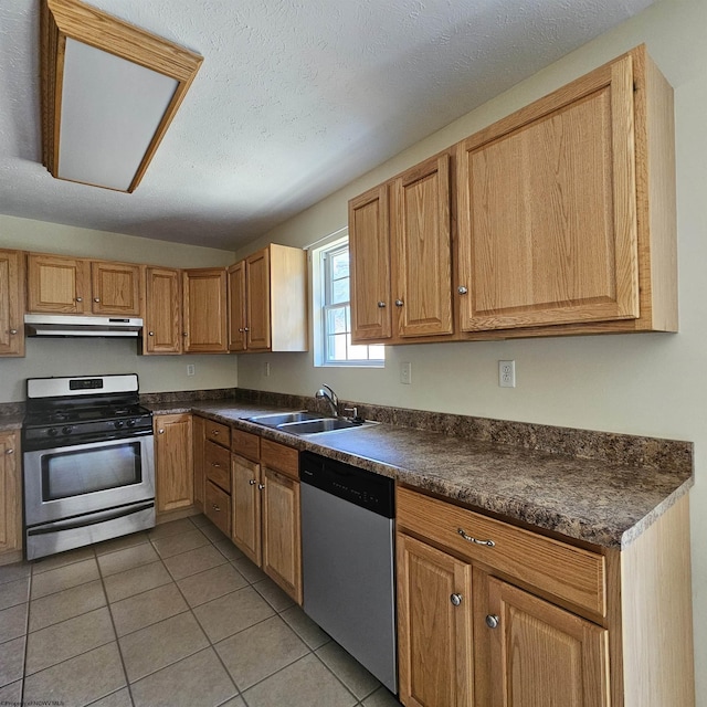 kitchen with light tile patterned floors, a sink, under cabinet range hood, appliances with stainless steel finishes, and dark countertops