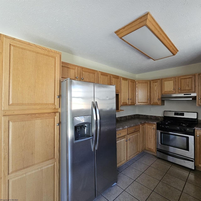 kitchen featuring dark tile patterned flooring, under cabinet range hood, dark countertops, a textured ceiling, and appliances with stainless steel finishes