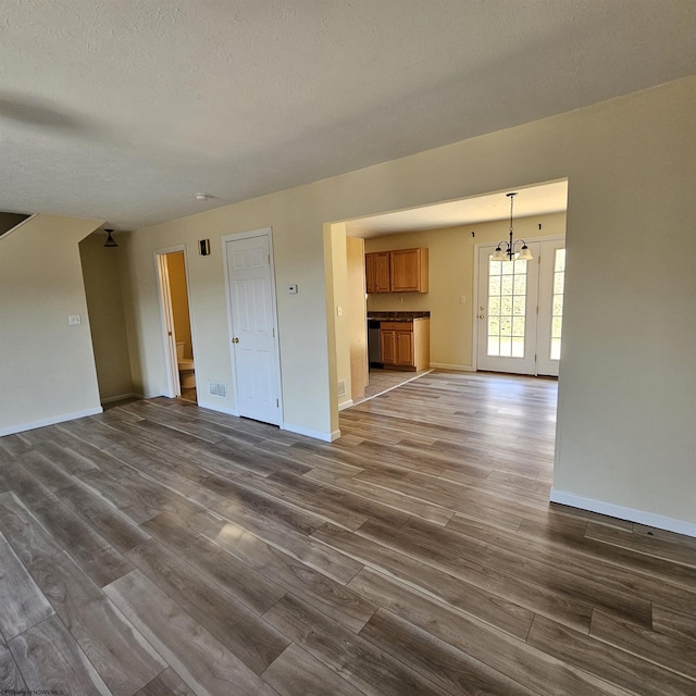 unfurnished living room featuring baseboards, a textured ceiling, a chandelier, and dark wood-style flooring