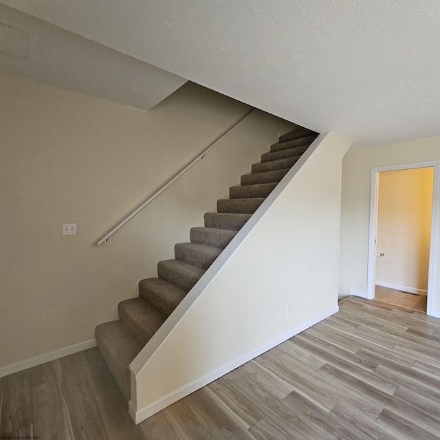 staircase with wood finished floors, baseboards, and a textured ceiling