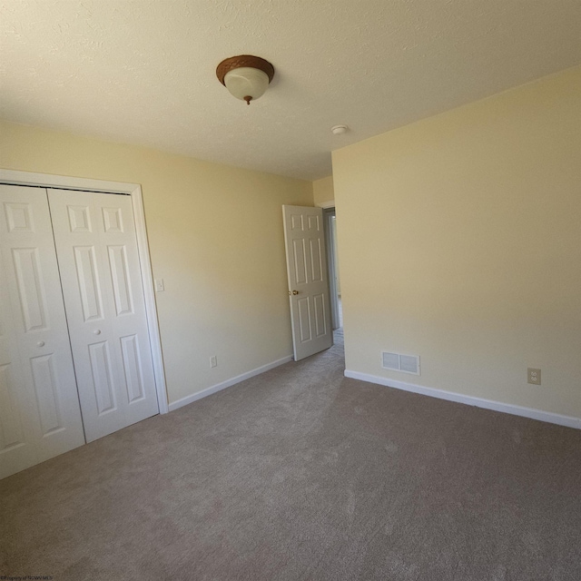 unfurnished bedroom featuring visible vents, a textured ceiling, a closet, carpet, and baseboards