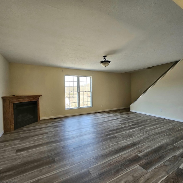 unfurnished living room with dark wood finished floors, a fireplace, a textured ceiling, and baseboards