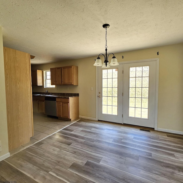 kitchen with dark countertops, wood finished floors, an inviting chandelier, brown cabinetry, and dishwasher