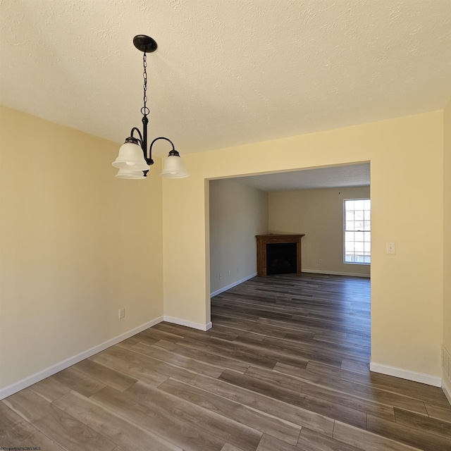 unfurnished dining area featuring a notable chandelier, a fireplace, baseboards, and dark wood-style flooring