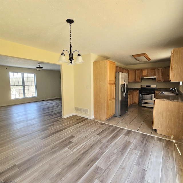 kitchen featuring dark countertops, under cabinet range hood, open floor plan, stainless steel appliances, and a sink