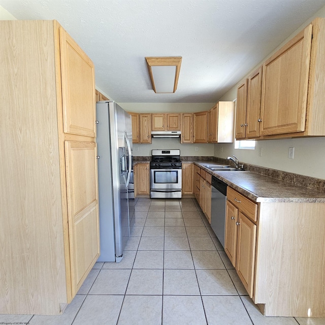 kitchen featuring dark countertops, under cabinet range hood, light tile patterned flooring, stainless steel appliances, and a sink