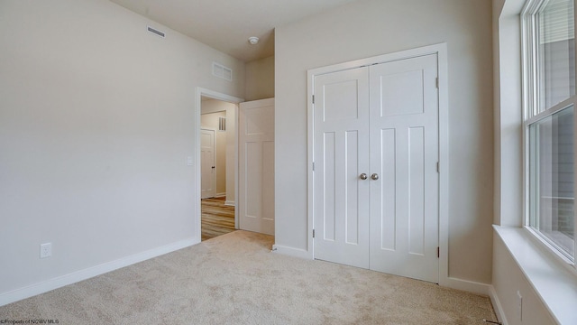 unfurnished bedroom with multiple windows, carpet flooring, visible vents, and a closet