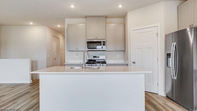 kitchen featuring a kitchen island with sink, appliances with stainless steel finishes, light wood-style floors, and a sink