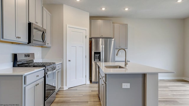 kitchen featuring gray cabinetry, an island with sink, appliances with stainless steel finishes, light wood-style floors, and a sink