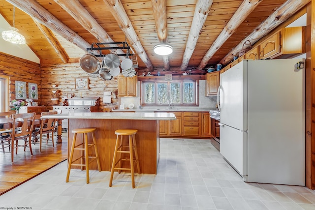 kitchen with beam ceiling, freestanding refrigerator, a breakfast bar area, light countertops, and range