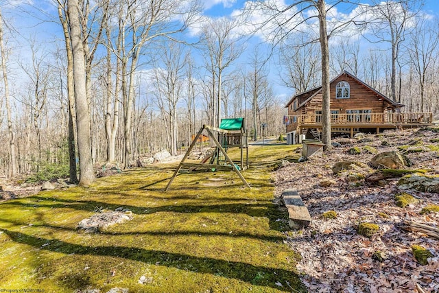 view of yard with a forest view, a deck, and a playground