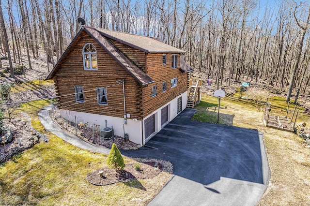 view of side of home featuring aphalt driveway, central AC, roof with shingles, an attached garage, and log exterior