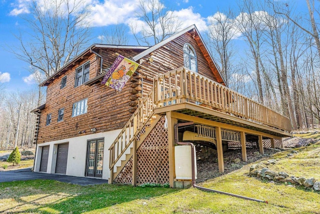 view of side of home with aphalt driveway, a yard, a wooden deck, log siding, and stairs