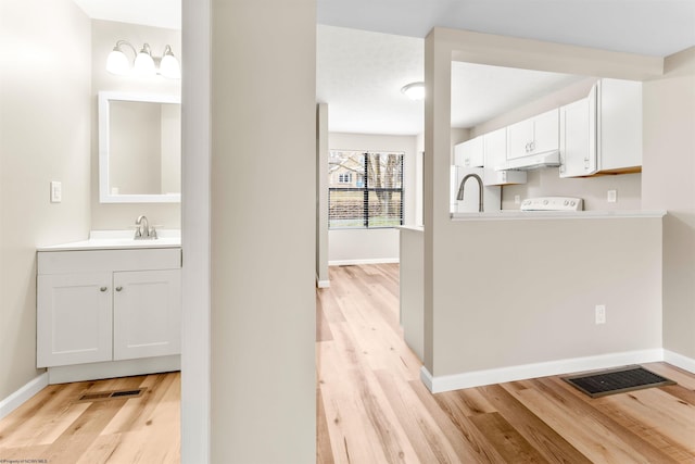 kitchen featuring visible vents, baseboards, under cabinet range hood, light wood-style flooring, and a sink