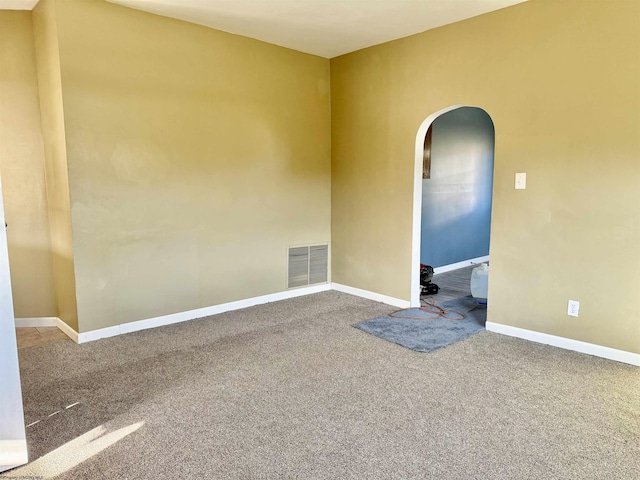 empty room with arched walkways, visible vents, baseboards, and carpet floors