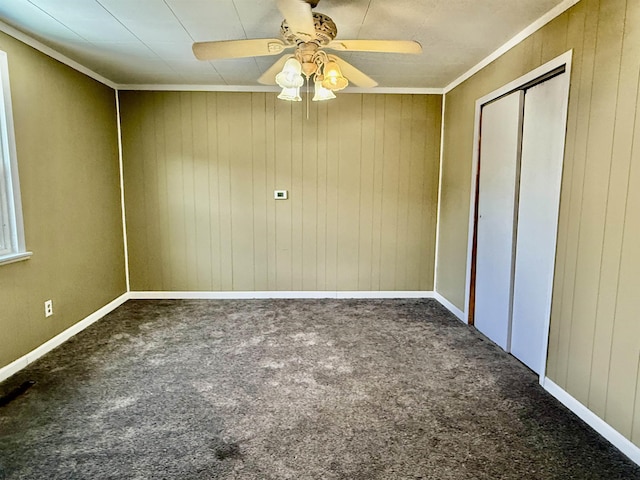 unfurnished bedroom featuring a closet, wooden walls, carpet flooring, crown molding, and ceiling fan