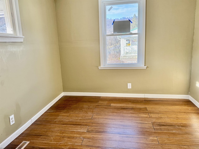 empty room featuring a wealth of natural light, visible vents, baseboards, and hardwood / wood-style flooring