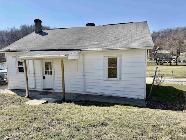 rear view of house with a lawn, fence, roof with shingles, and a chimney