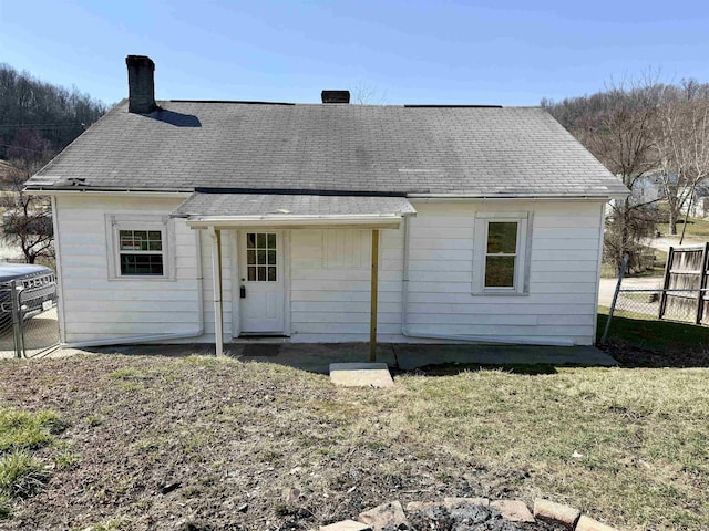 rear view of property with fence, a lawn, roof with shingles, and a chimney