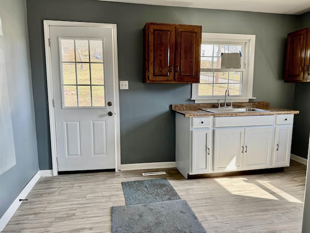 kitchen featuring a sink, baseboards, light wood-style flooring, and white cabinets