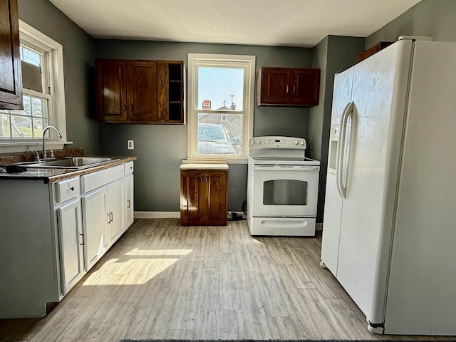 kitchen with dark countertops, baseboards, light wood-type flooring, white appliances, and a sink