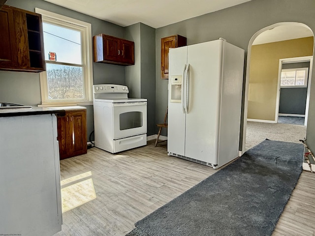 kitchen with arched walkways, light wood finished floors, white appliances, and baseboards