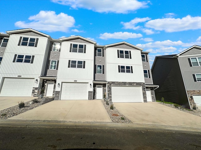 townhome / multi-family property with a garage, stone siding, and driveway