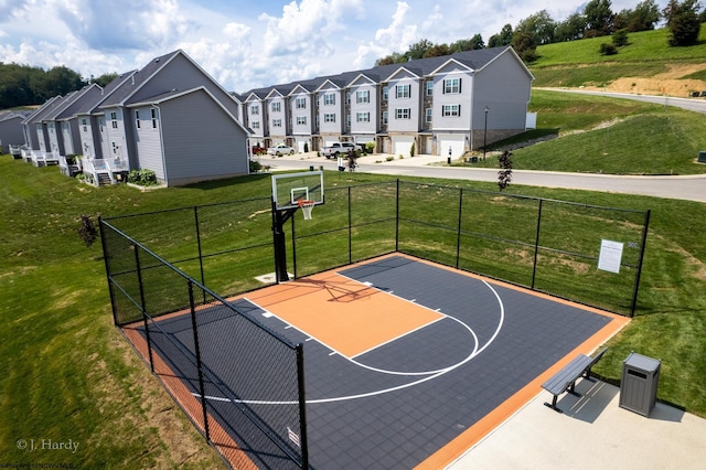 view of sport court with basketball hoop, a yard, fence, and a residential view