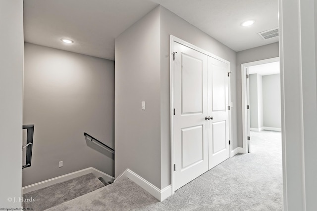 hallway with carpet flooring, an upstairs landing, visible vents, and baseboards