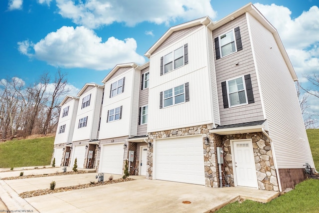 townhome / multi-family property featuring a garage, stone siding, and driveway