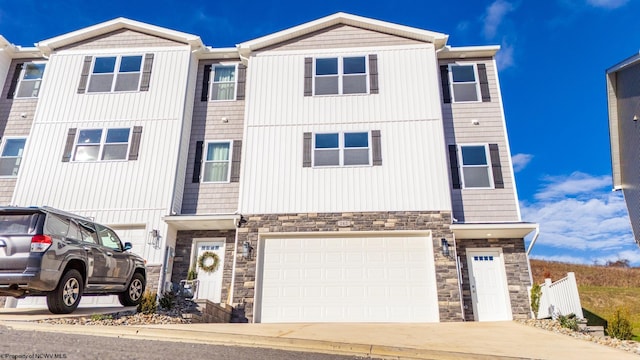 townhome / multi-family property with a garage, stone siding, and driveway