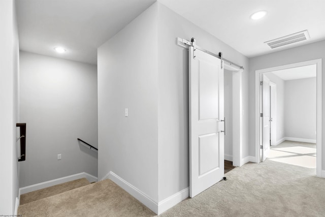 hallway with visible vents, baseboards, carpet, a barn door, and an upstairs landing