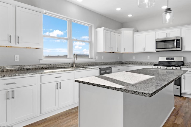 kitchen with light stone counters, wood finished floors, a center island, appliances with stainless steel finishes, and white cabinets